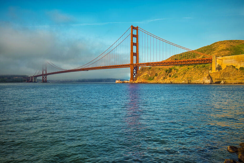 Golden Gate Bridge over calm blue sea with sunlit hills and vivid sky wallpaper background
