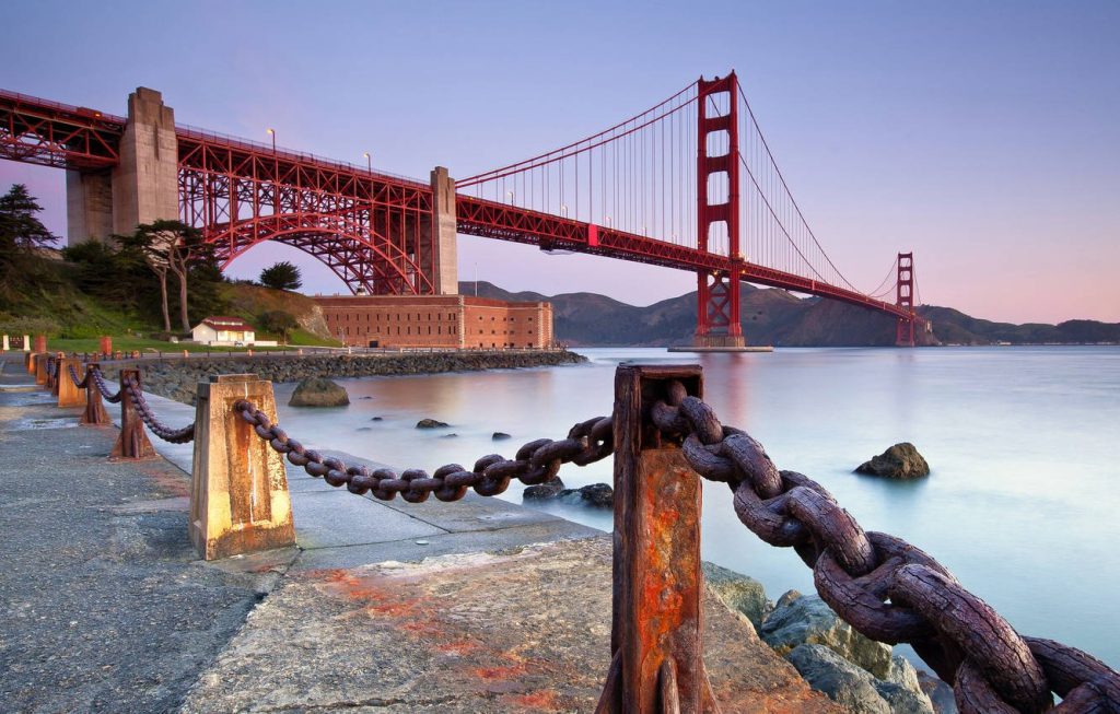 Golden Gate Bridge at dusk framed by rusted iron chains and historic Fort Point scenic wallpaper