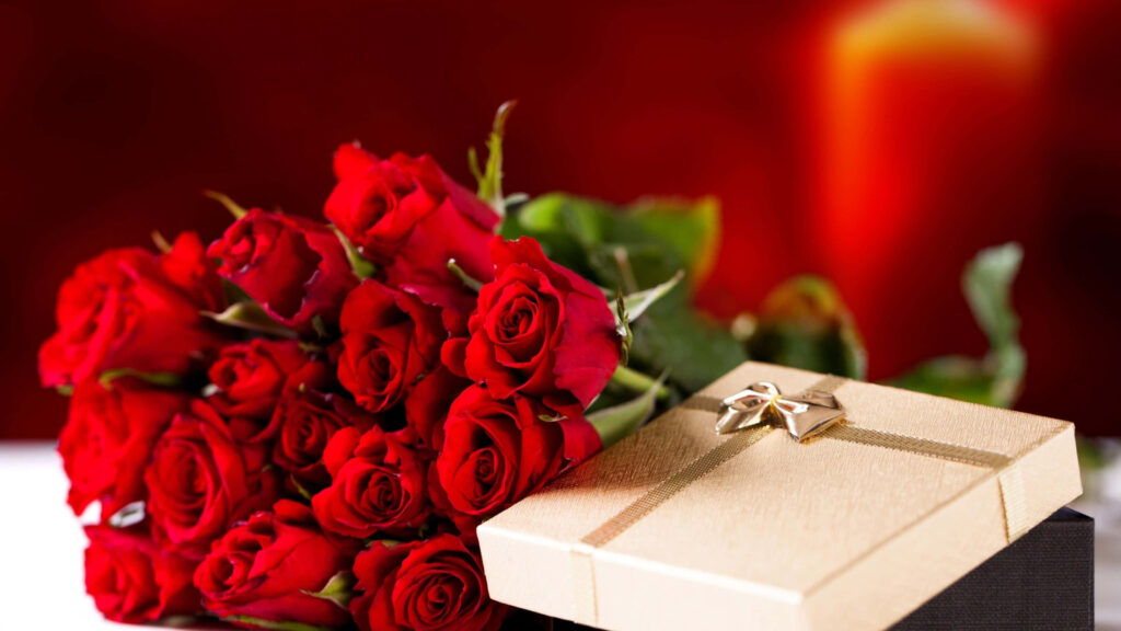 Golden gift box with star detail beside vibrant red roses on warm romantic wallpaper background