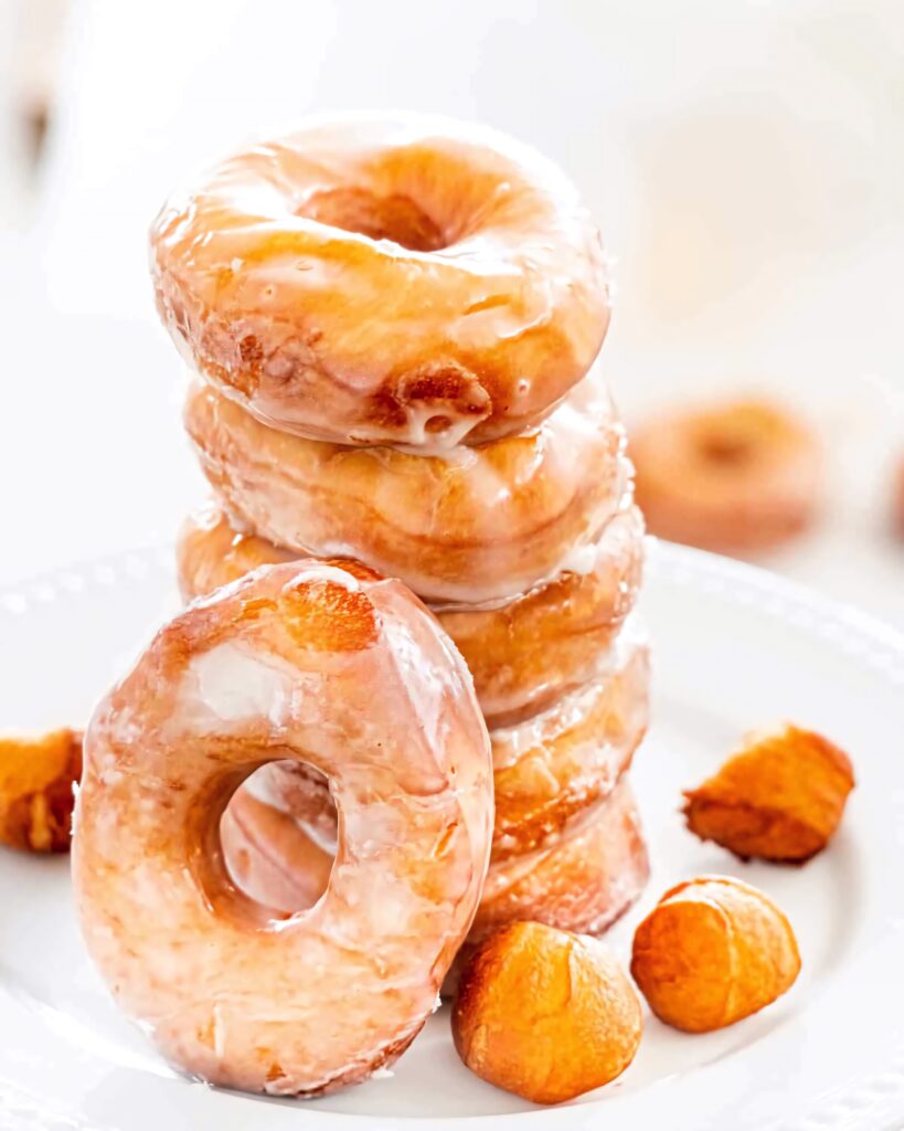 Stack of golden glazed donuts on white plate with glossy sheen fresh fluffy texture wallpaper