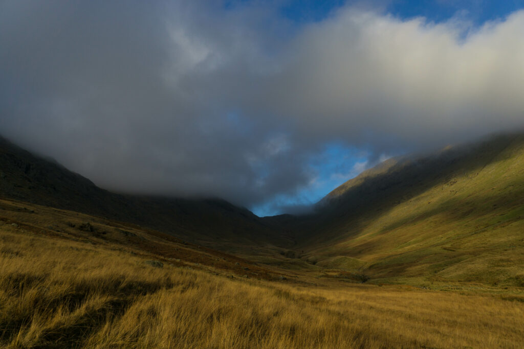 Serene valley with golden grass hills under soft clouds and sunlight for nature wallpaper background