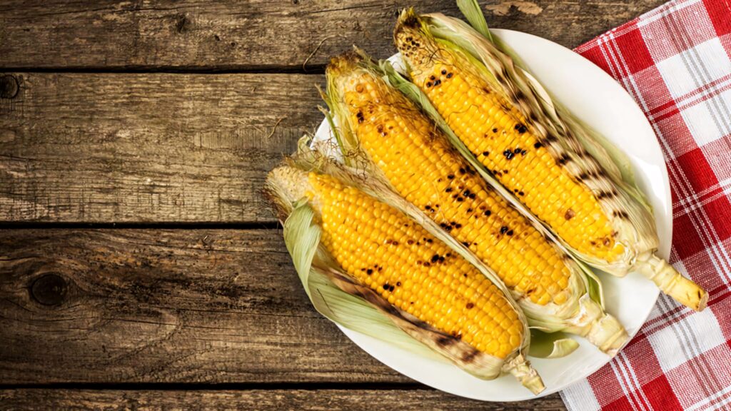 Golden grilled corn on the cob on white plate with checkered cloth rustic summer picnic scene Wallpaper
