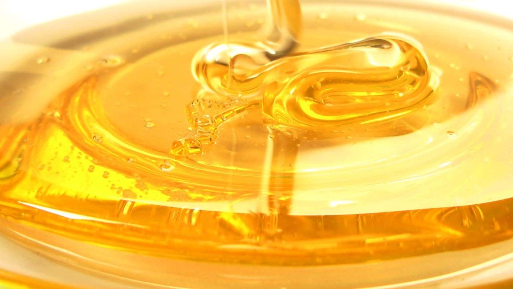 Macro close-up of golden honey dripping into a warm sunlit pool with smooth viscous texture Wallpaper