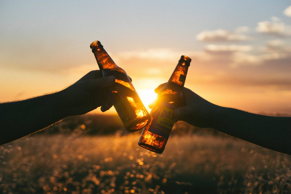 Two hands clinking Dad's Old Fashioned Root Beer bottles at sunset cozy outdoor moment wallpaper