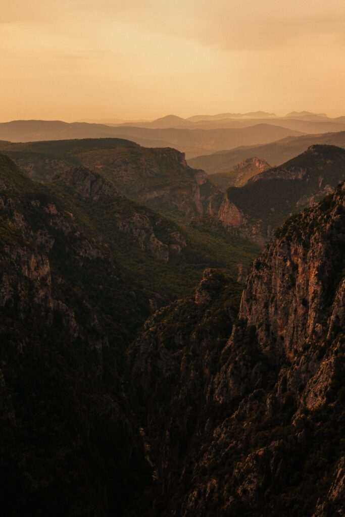 Rugged rocks and towering mountain peaks with rolling hills under warm golden light wallpaper