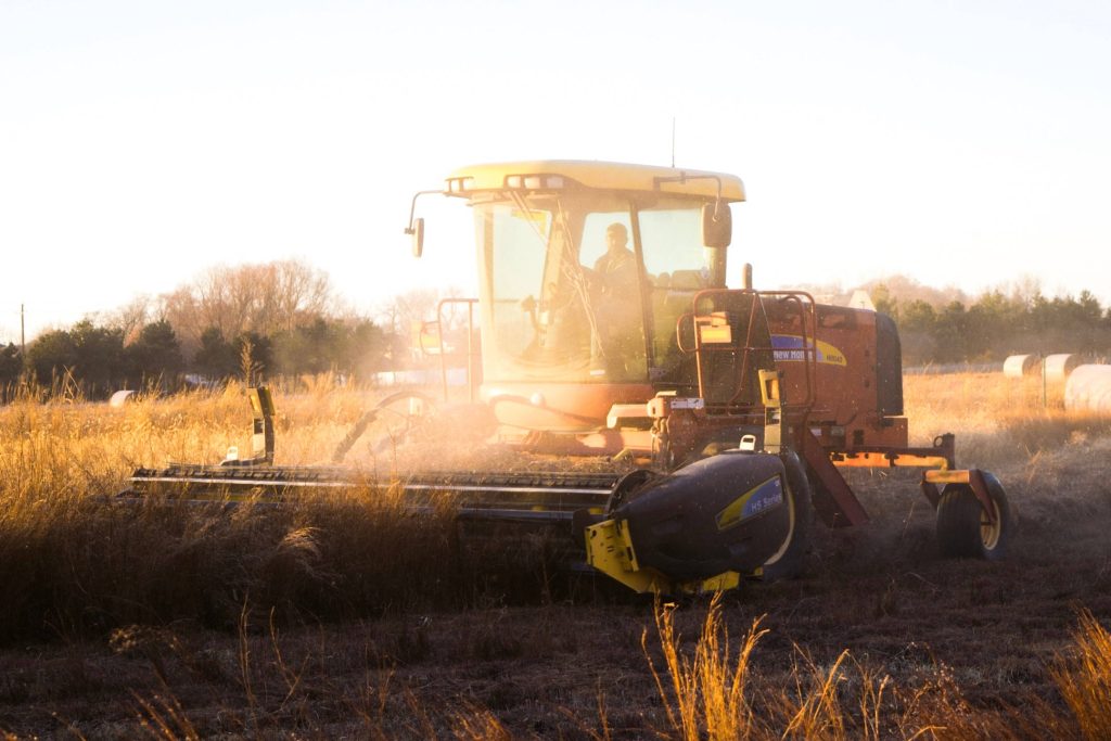 New Holland windrower harvesting dry grass at golden hour in rustic farm field with warm sun Wallpaper