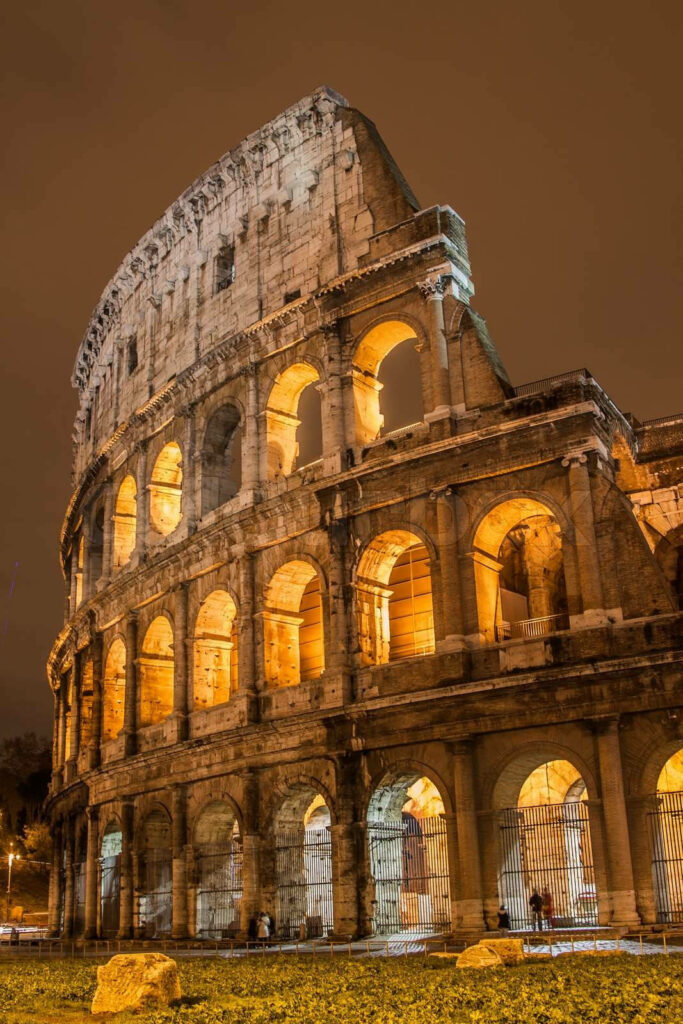 Roman Colosseum illuminated in golden light with intricate arches against a brown sky wallpaper