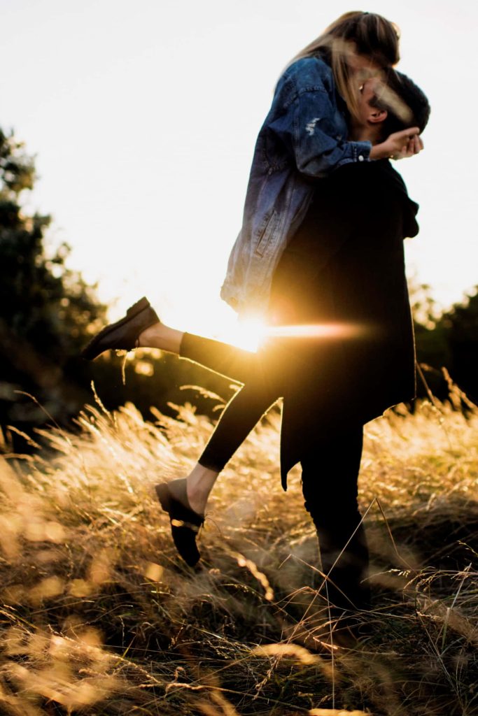 Young couple sharing loving kiss in sunlit field golden hour romantic wallpaper background