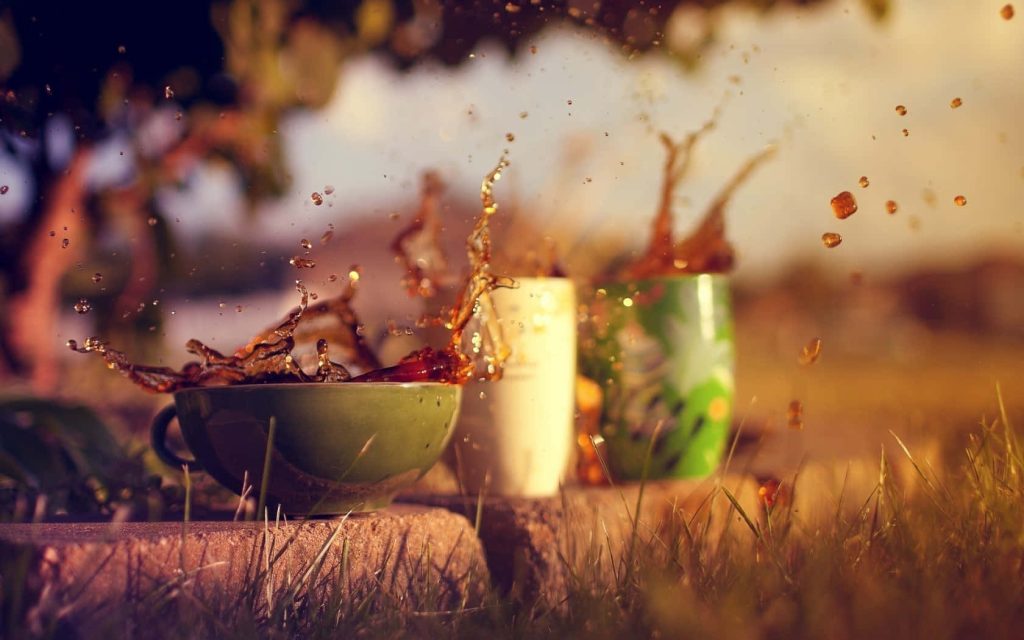 Green mug splashing liquid outdoors on grass with golden hour light vibrant caffeine wallpaper