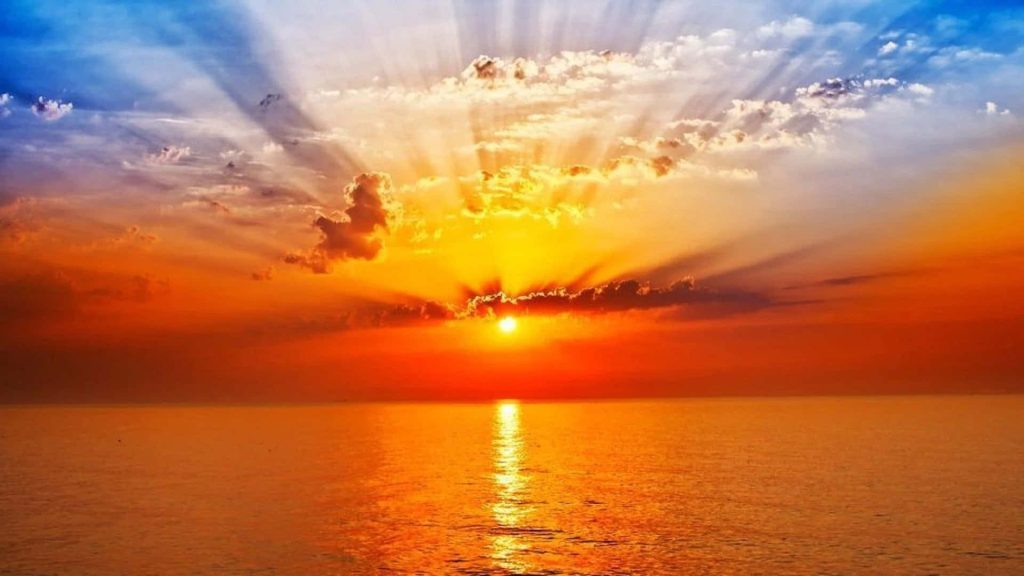 Golden hour sunset over calm ocean with crepuscular rays and vibrant orange sky wallpaper