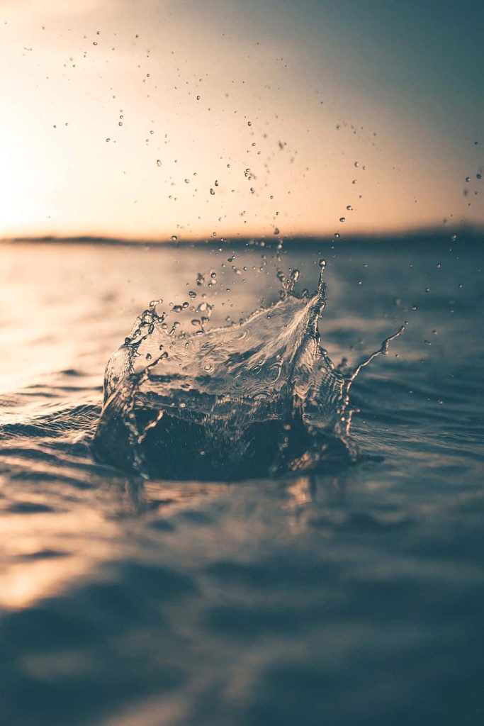 Water splash with golden hour light reflecting on calm deep water creating dynamic ripples Wallpaper