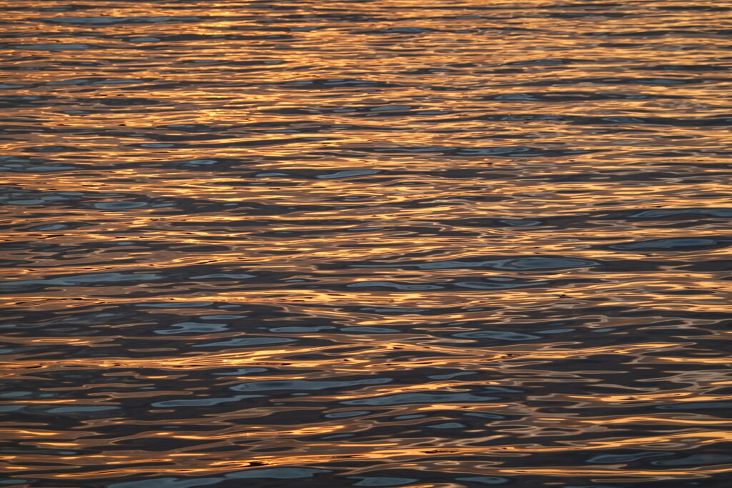 Serene lake wallpaper with golden light reflections on gently wavy water for calm background
