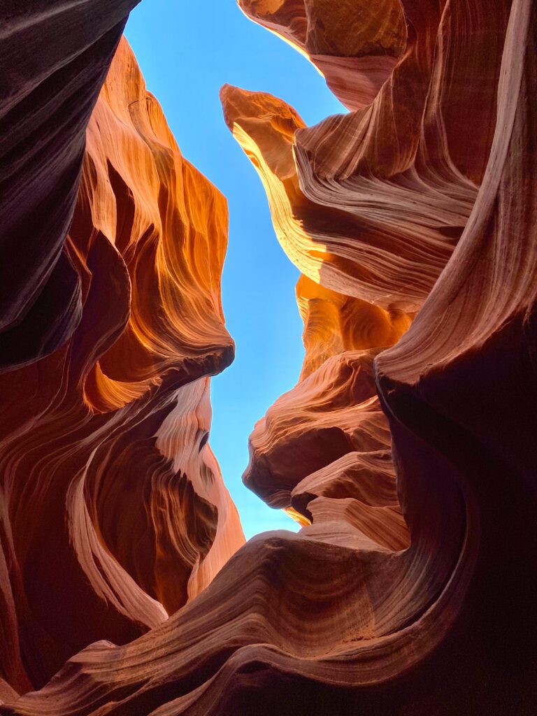 Cave interior with sculpted rocks sandy floor warm golden light and vivid blue sky landscape wallpaper