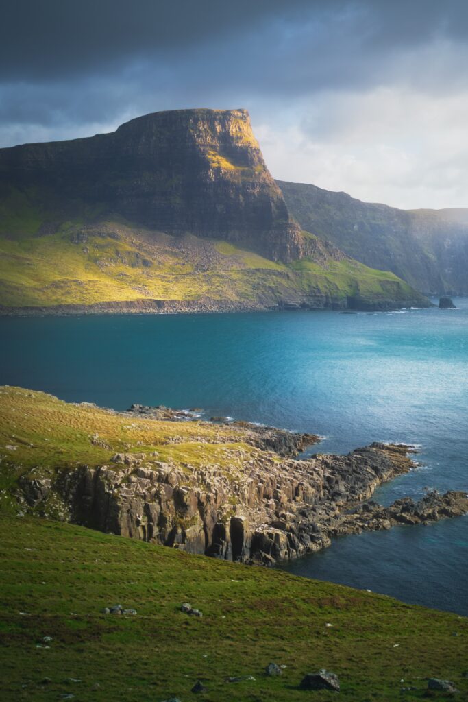 Dramatic coastal cliff with golden light turquoise sea lush green shores rocky outcrops wallpaper