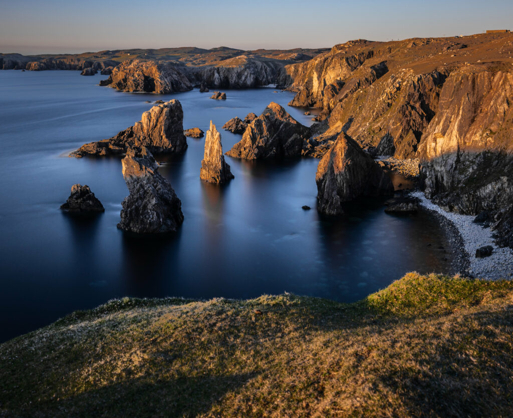 Rugged coastal landscape with golden light rock formations calm blue sea and textured hills wallpaper