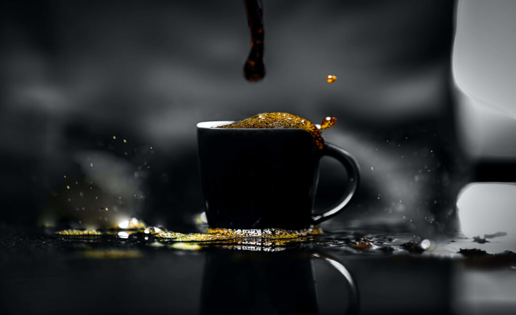 Close-up of black coffee cup with dynamic fresh coffee splash highlighted by golden light background Wallpaper