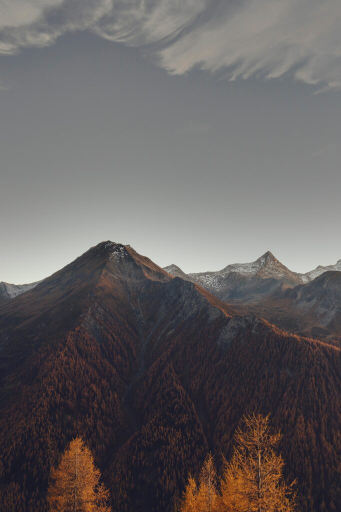 Majestic mountain range with autumn forests and dramatic clouds in warm golden light wallpaper