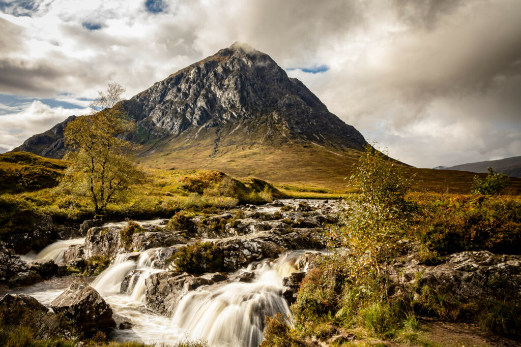 Golden sunlight over river flowing through rocky terrain with lush trees and majestic mountain Wallpaper
