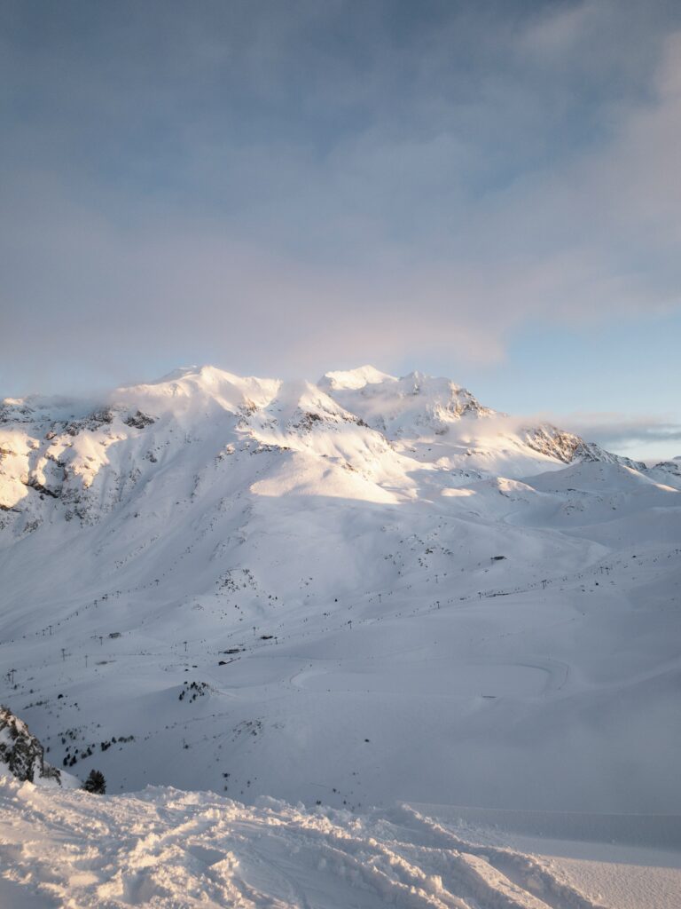 Snowy mountain peak bathed in golden light under cloudy sky serene winter alpine landscape wallpaper