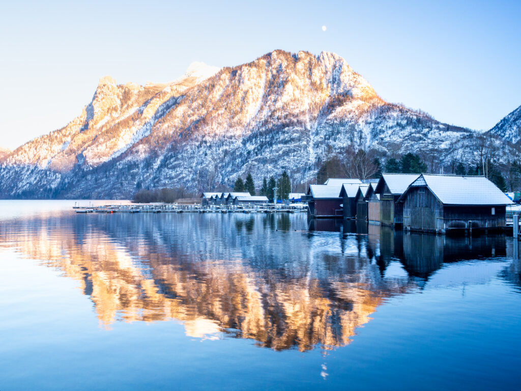 Snow-capped mountains golden light reflecting on crystal clear lake by peaceful lakeside houses Wallpaper