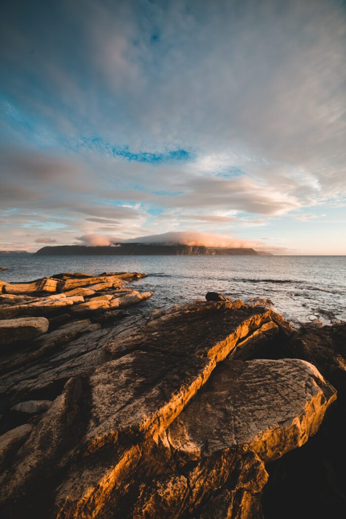Golden light illuminates rugged coastal rocks with misty fog and soft clouds over the sea Wallpaper