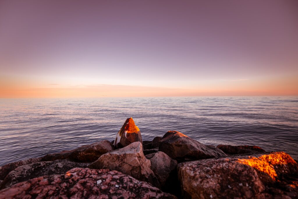 Golden light on rugged rocks by calm sea with violet and orange gradient sky wallpaper background