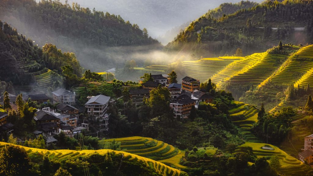 Golden morning light on misty Longji Rice Terraces and traditional village in Guangxi China Wallpaper