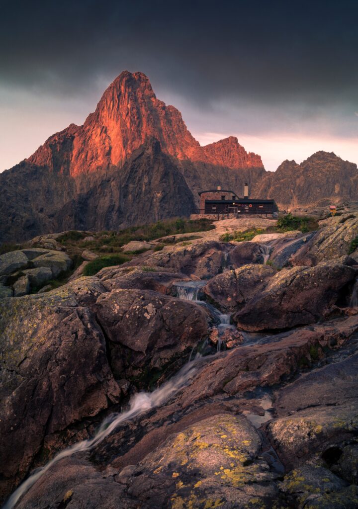 Mountain landscape wallpaper with cozy house rugged rocks gentle stream and golden light peak