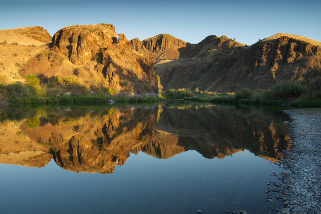 Golden mountains and rugged peaks reflected in calm lake waters under clear blue skies Wallpaper