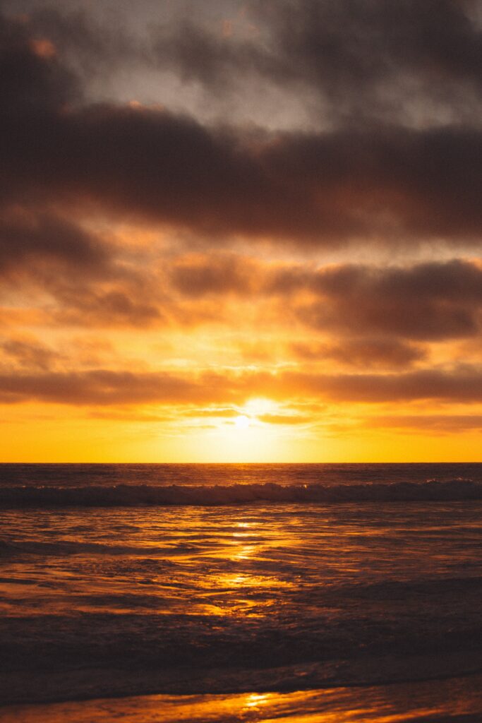 Sunset over ocean with golden reflections dramatic clouds and tranquil warm glow wallpaper background