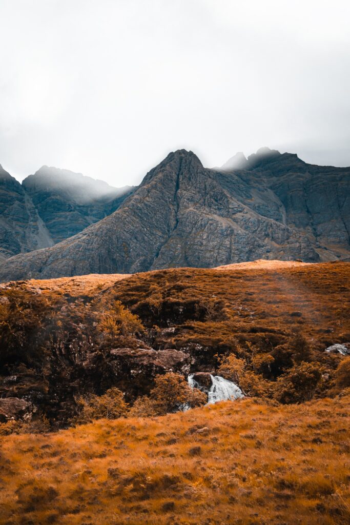 Stunning wallpaper of rugged mountains with rocky peaks and golden orange landscape foreground
