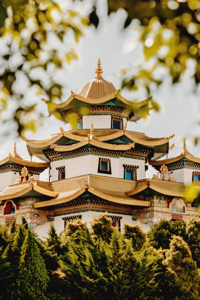 Pagoda-style building with gold accents surrounded by lush green trees in sunlit nature background Wallpaper