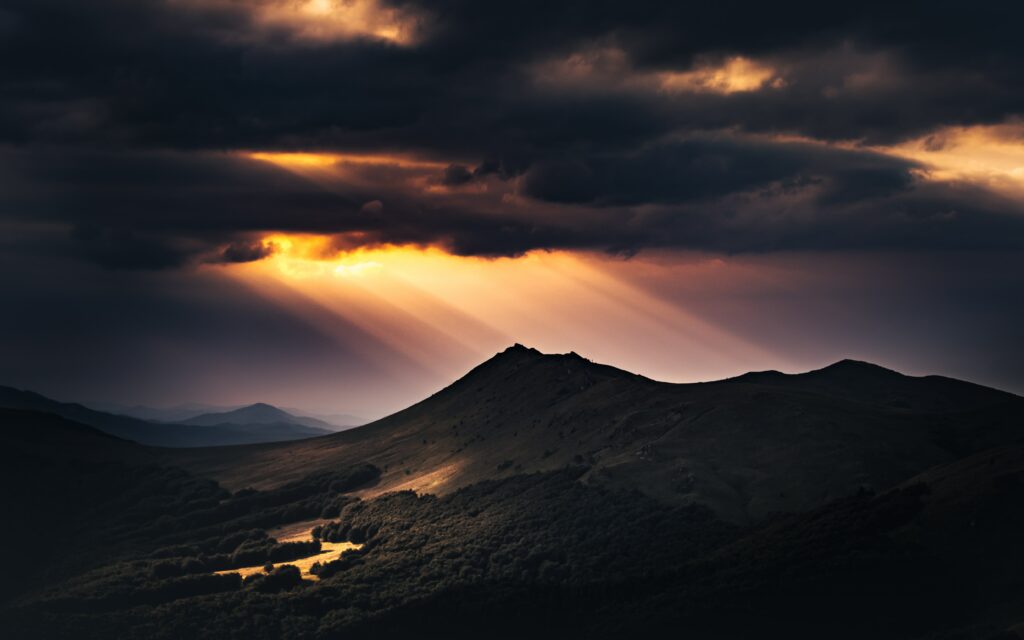 Dramatic mountain landscape with golden sunlight breaking through dark moody clouds wallpaper
