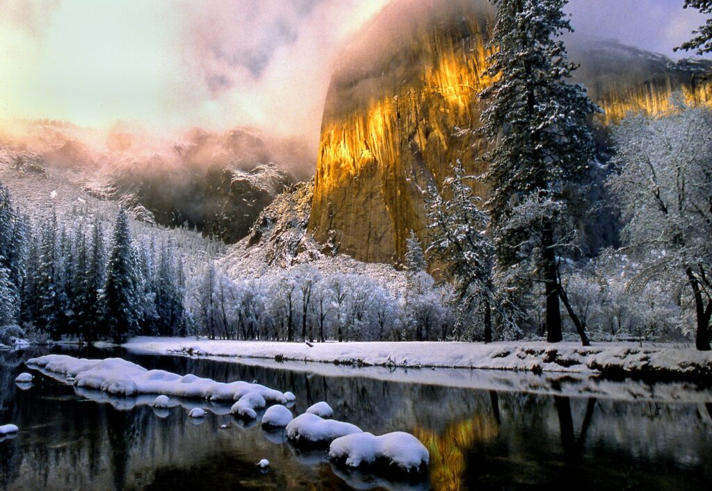 Snowy landscape with golden illuminated rock evergreen trees by calm lake serene winter wallpaper