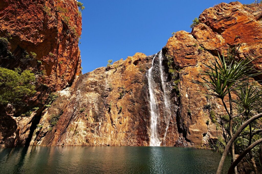 Waterfall cascading over golden rocks with palm trees under bright blue sky nature wallpaper background