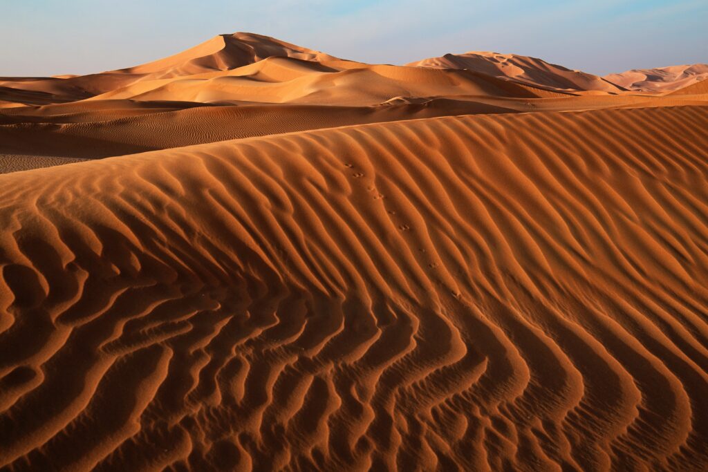 Golden sand dunes with intricate patterns under clear blue sky in serene desert landscape Wallpaper