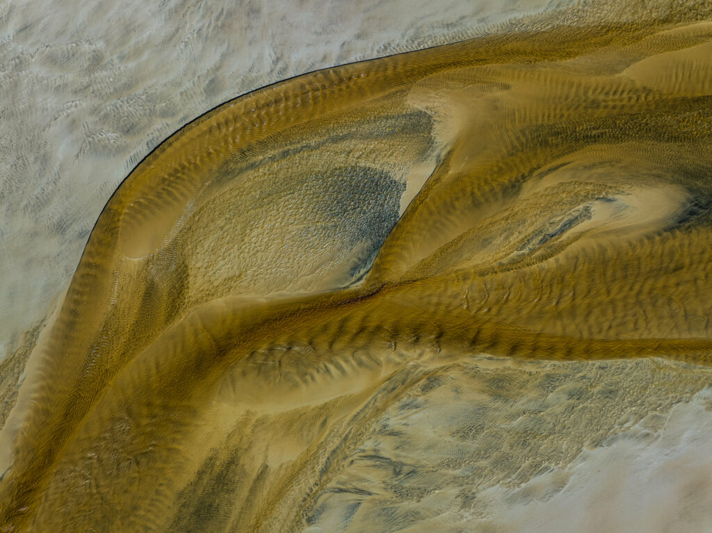 Aerial view of beach with golden sand and shallow water creating natural abstract patterns wallpaper