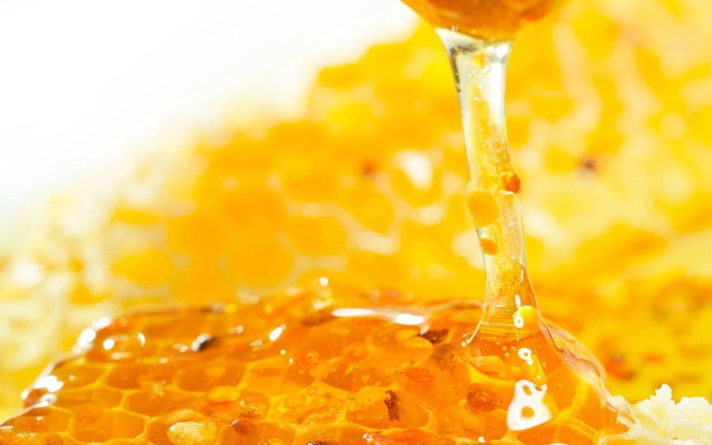 Macro photo of golden raw honey dripping onto textured honeycomb with warm amber hues wallpaper