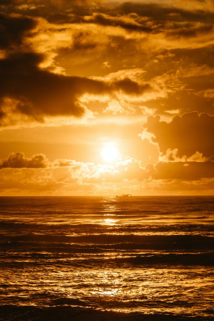 Golden sun setting over water with radiant rays and dark clouds in dramatic seascape wallpaper