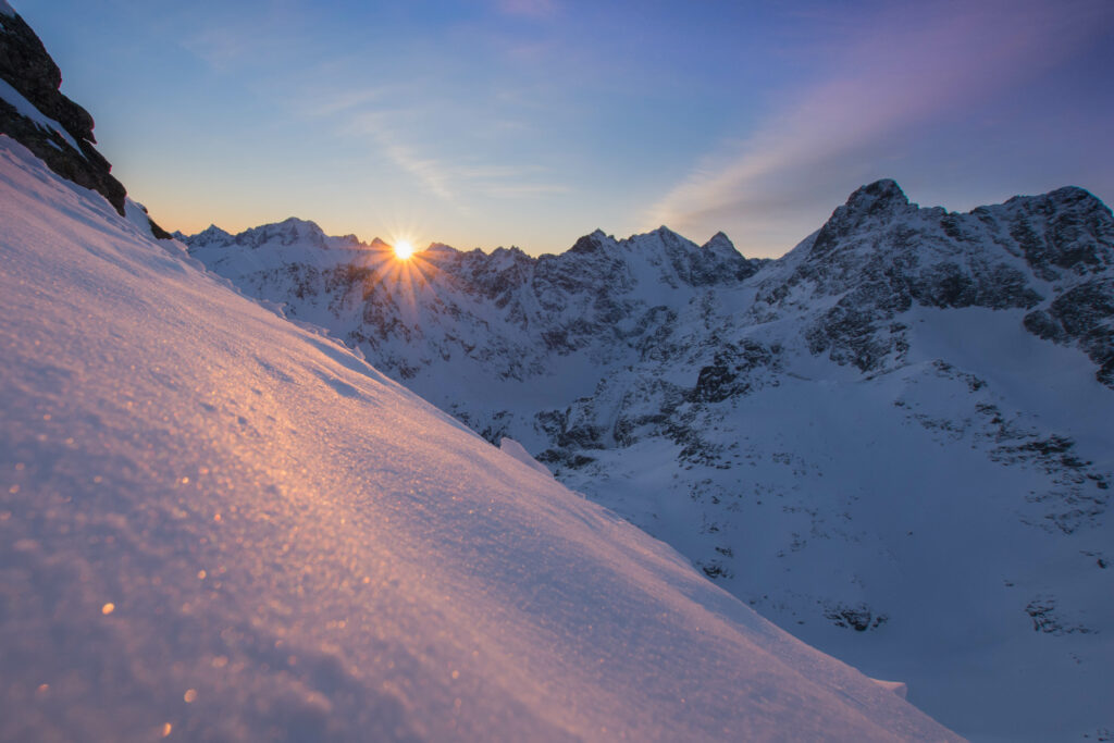 Golden sun rays shine over snow-covered rugged mountain peaks in a serene winter alpine landscape Wallpaper