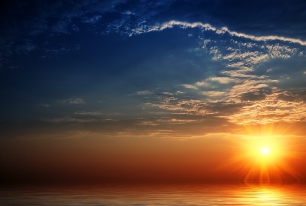 Sunlight beams through feathered clouds over calm water with golden light and deep blue sky Wallpaper