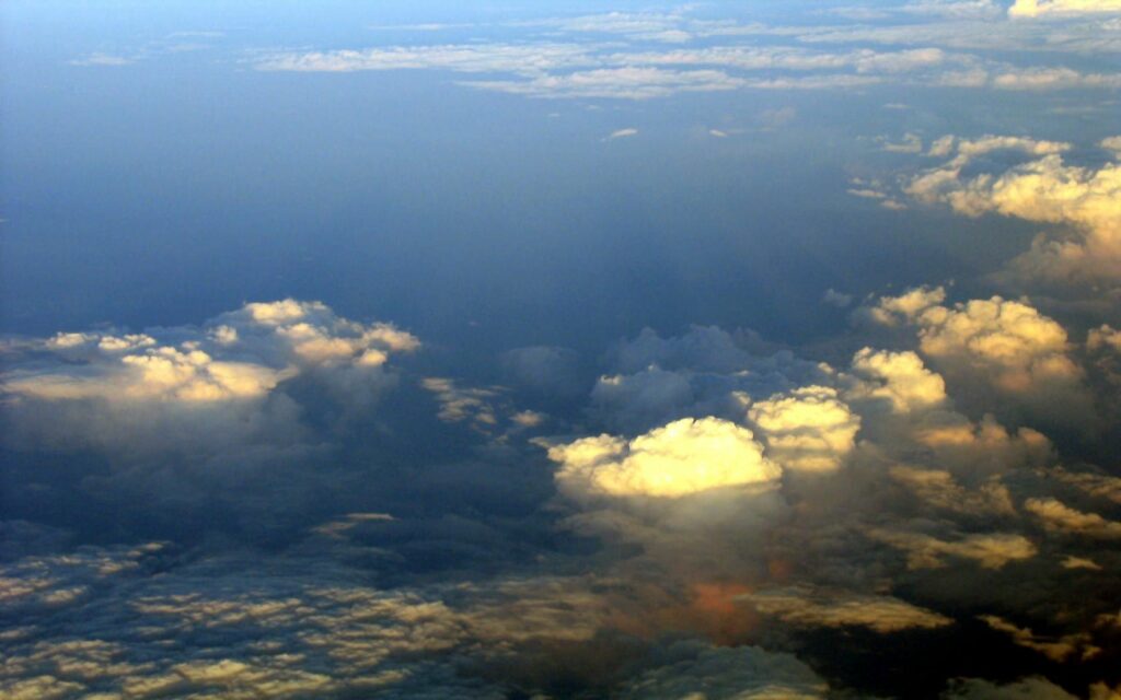 Aerial view above clouds with golden sunlight and soft shadows serene sky wallpaper background