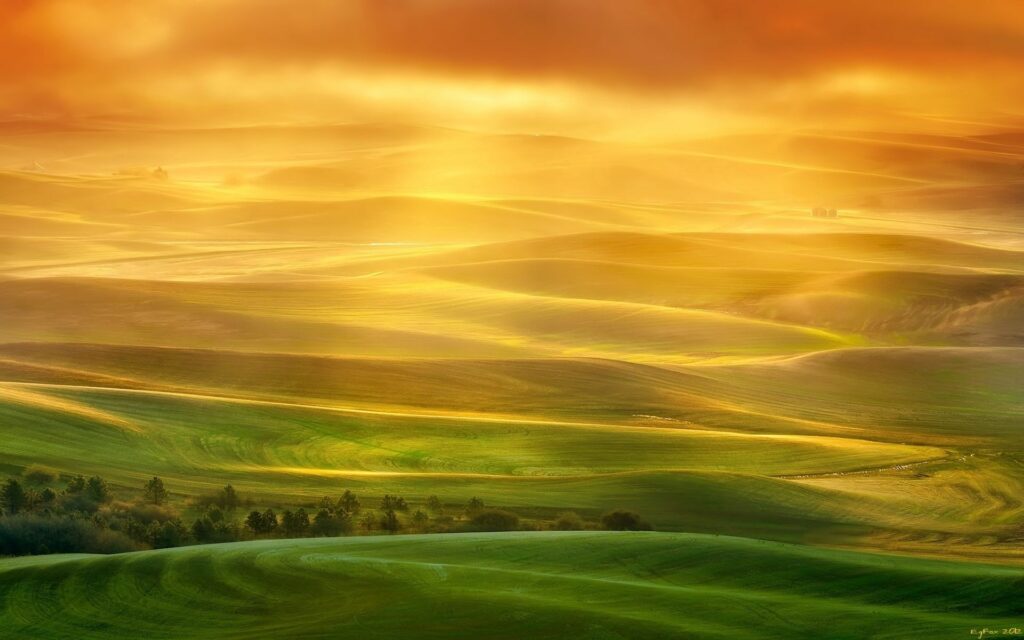 Golden sunlight illuminates rolling fields and plateaus with warm orange and green hues at sunset Wallpaper