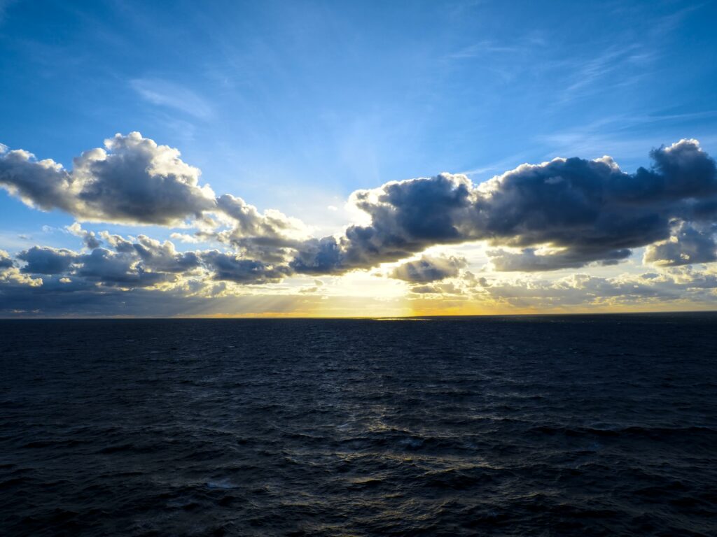Vibrant ocean horizon with golden sunlight through clouds peaceful seascape wallpaper background