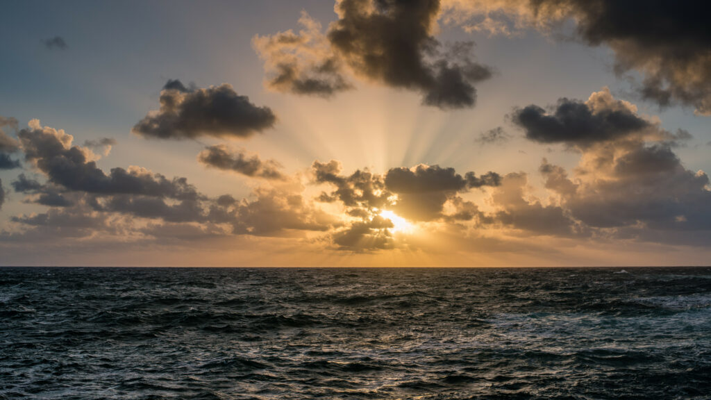 Dynamic sea waves under dramatic clouds with golden sunlight creating a serene seascape wallpaper
