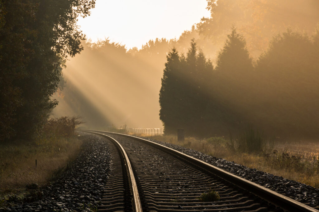 Sunlight piercing dense fog over quiet railroad tracks surrounded by lush green trees landscape Wallpaper