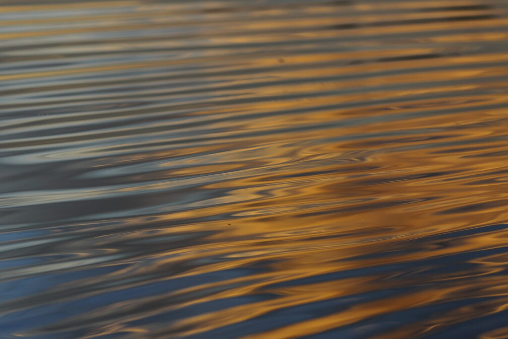 Golden sunlight reflections on gentle blue water waves creating a calming abstract wallpaper background