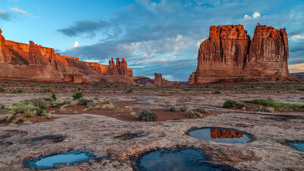 Golden sunlight on Arches National Park rock formations with reflective water and desert landscape Wallpaper