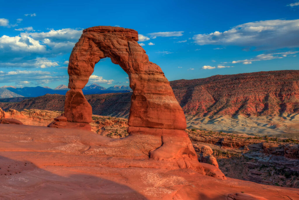 Delicate Arch glowing in warm sunlight red sandstone Utah landscape vivid blue sky background Wallpaper