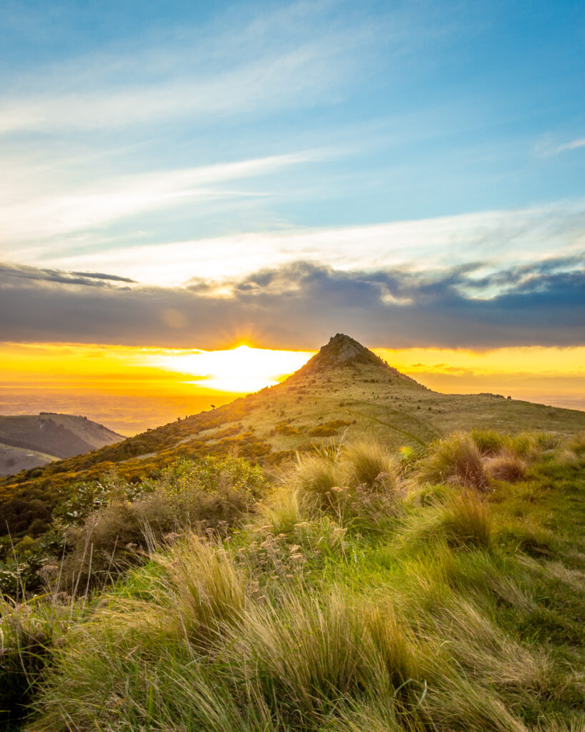Golden sunlight on grassy slope and mountain peak under vibrant sunset sky wallpaper background